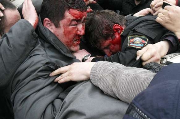 Zbitý policista se snaží ochránit v davu demonstrantů.