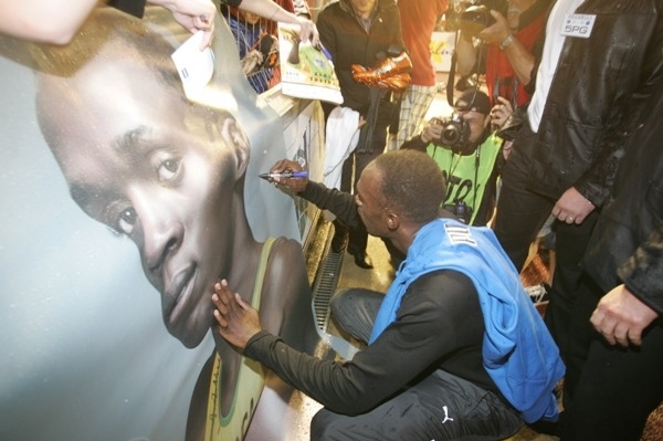 Usain Bolt se podepisuje na plakát fanouškům.