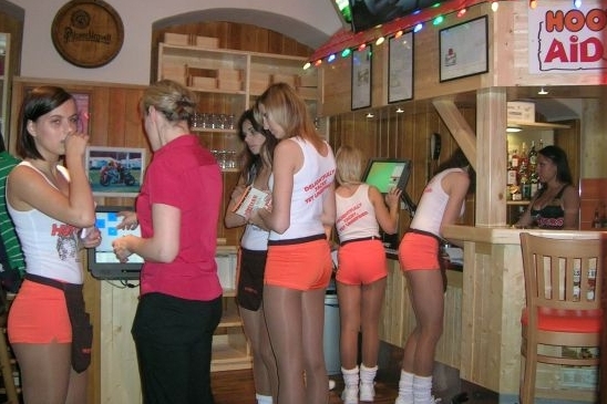 V Hooters vás obslouží dívky v oranžových kraťasech a bílém tílku.