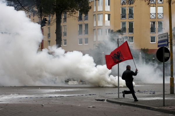Demonstrant běží ulicí s albánskou vlajkou.