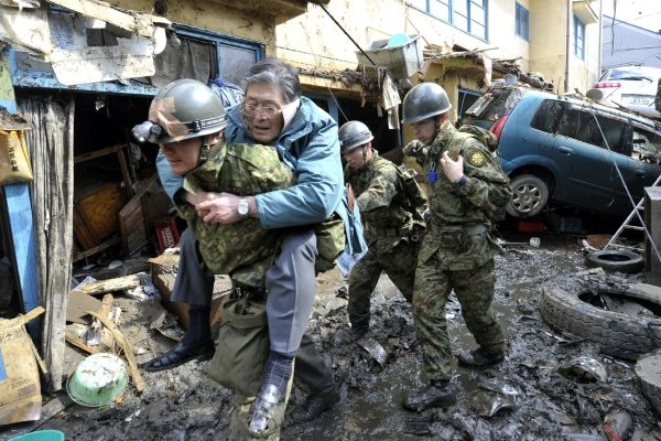 Japonští záchranáři vynášejí ze zničené oblasti přeživší.