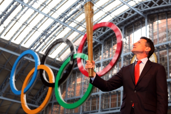 Předseda organizačního výboru Sebastian Coe pózuje s pochodní před olympijskými kruhy.