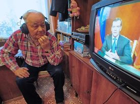 Starší Rus sleduje v TV předvolební kampaň.