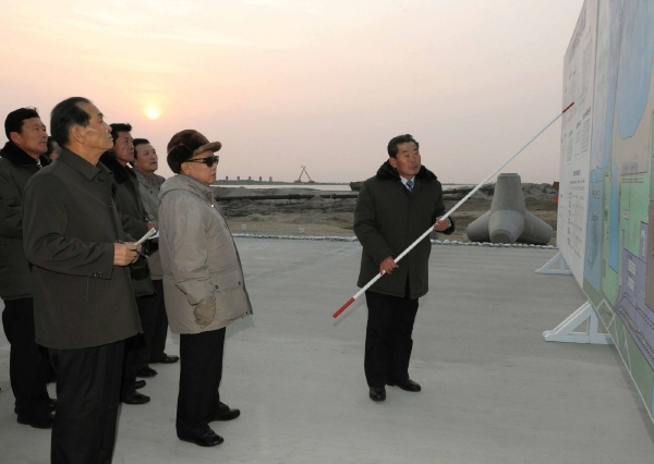 Kim Čong-il koukající na obří tabuli.