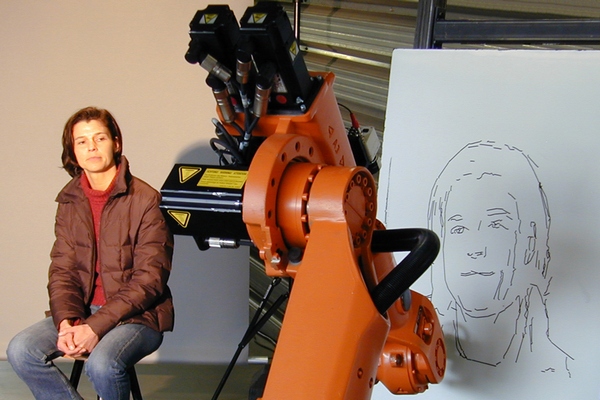 Robot si člověka nejprve vyfotografuje, potom načrtne jeho portrét. Robot si člověka nejprve vyfotografuje, potom načrtne jeho portrét.
