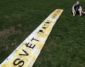 Účastník protestního shromáždění Společně za změnu! Chceme skutečnou demokracii! sedí u transparentu s nápisem "Svět patří nám všem".