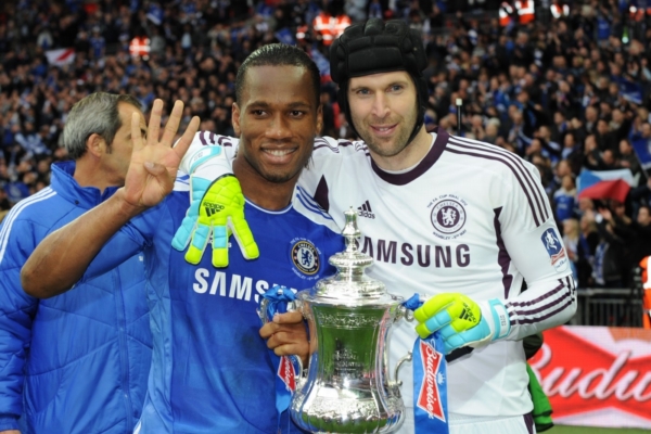 Petr Čech a Didier Drogba s pohárem na prstech ruky ukazují, kolikátý FA Cup v Chelsea vyhráli.