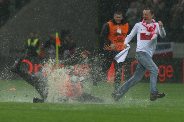 Fanoušek utíká před pořadatelem, který se poté vymáchal v jedné z louží na trávníku.