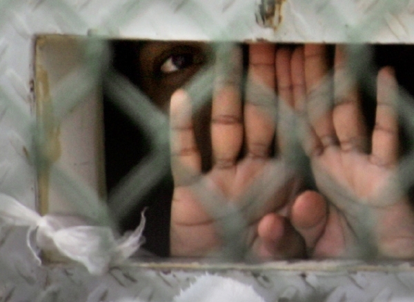 Fotografie vězně v zálivu Guantánamo, který se dívá ven tzv. fazolovou dírou. Používá se k předávání jídla. 