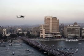 Vojenská helikoptéra letí nad demonstranty na mostě, který vede k náměstí Tahrir v Káhiře.