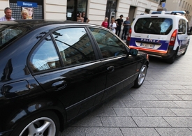 Policie odváží zlatníka, kterého přepadli. Sedí v tmavém autě.