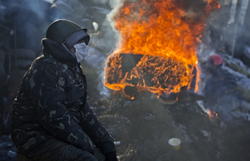 Demonstrant sedí vedle hořící barikády v centru Kyjeva.