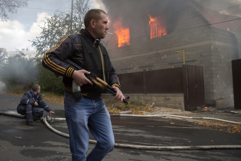 Proruský rebel prochází kolem hořícího domu ve městě Doněck 5. října 2014. Proruský rebel prochází kolem hořícího domu ve městě Doněck 5. října 2014.
