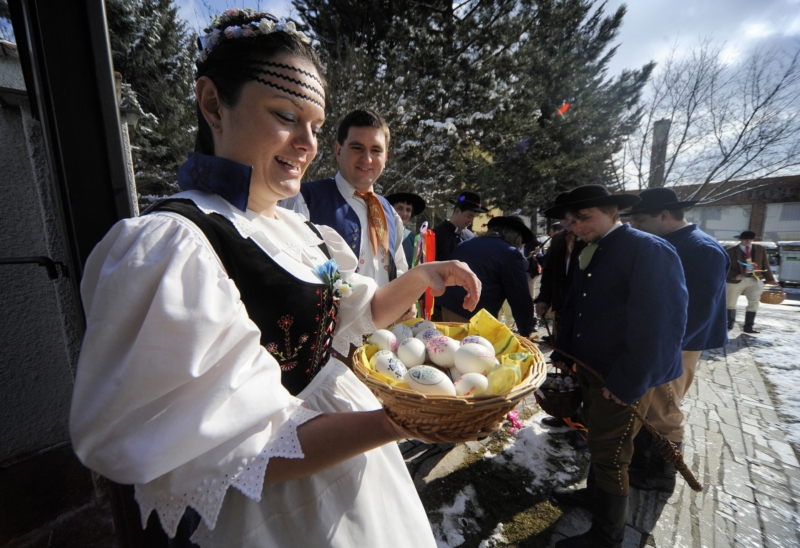 Dívka v kroji předává koledníkům kraslice (snímek z roku 2013).
