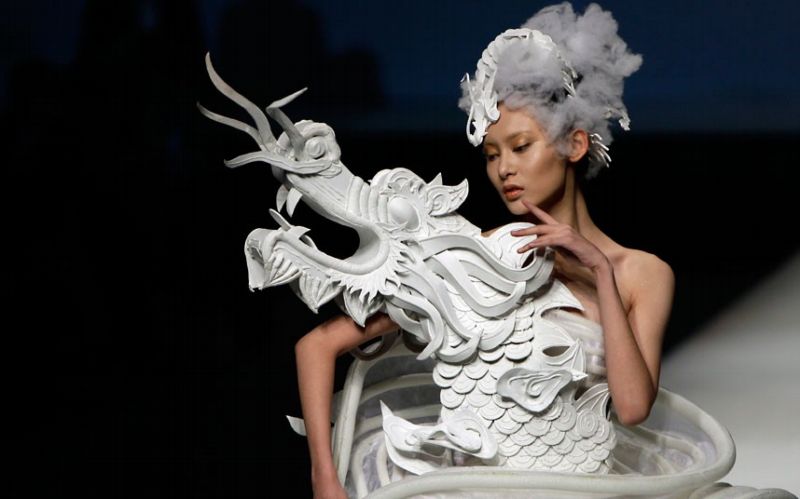 Modelka prezentuje šaty s drakem od Xu Minga na festivalu módy China Fashion Week v Pekingu.