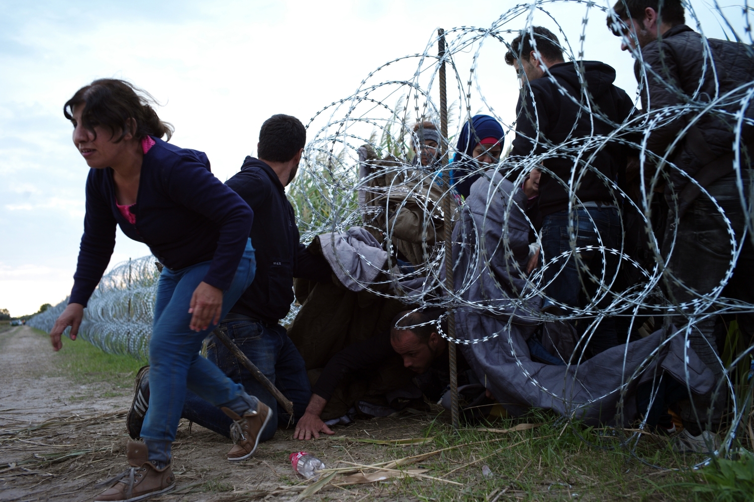 Migranti v Maďarsku prorážejí plotem z ostnatého drátu.