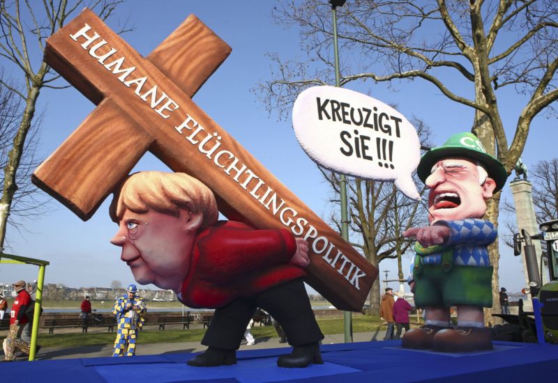 Sousoší navržené umělcem Jacquesem Tillym znázorňuje kancléřku Angelu Merkelovou s velkým dřevěným křížem na zádech s nápisem Humánní politika pro uprchlíky. Vedle ní je bavorský premiér Horst Seehofer, který jako kritik uprchlické politiky Merkelové ukazuje prstem na kancléřku, pláče a volá Ukřižovat!