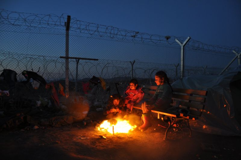 Migranti se hřejí u ohně.