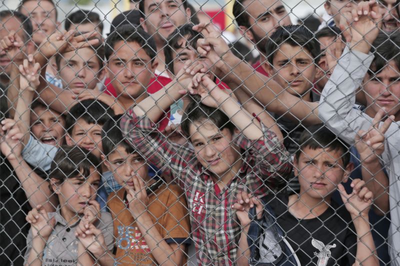Migranti stojící za plotem v uprchlickém táboře Nizip v jihovýchodním Turecku.