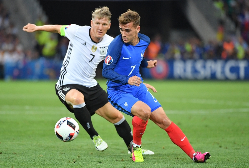 Šampion a smolař. Antoine Griezmann v souboji s Bastianem Schweinsteigerem (vlevo).