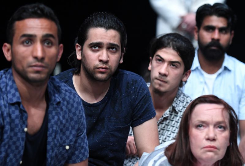 Migranti, kteří přišli do Německa. Na obrázku jsou zapojeni do divadelní hry, kde společně s evropskými aktivisty promlouvají o své cestě do Evropy. Hra jim má pomoci v začlenění do společnosti. V popředí německá herečka Martina Krompholzová.