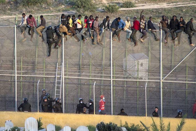 Hraniční plot a na něm migranti.