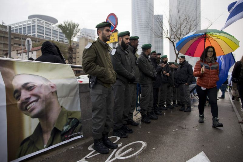 Případ Elora Azarii rozděluje Izrael. Na snímku vojenští policisté dohlížejí na demonstraci za podporu Azarii (jehož podobizna je na plakátu).