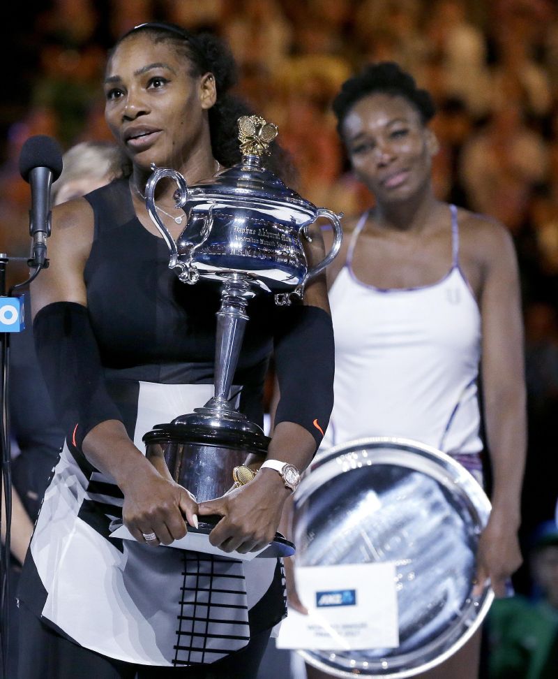 Serena Williamsová s pohárem, za ní její poražená sestra Venus.