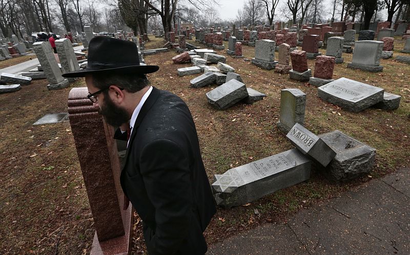 Muž kráčí kolem poničených náhrobků na židovském hřbitově v americkém St. Louis.