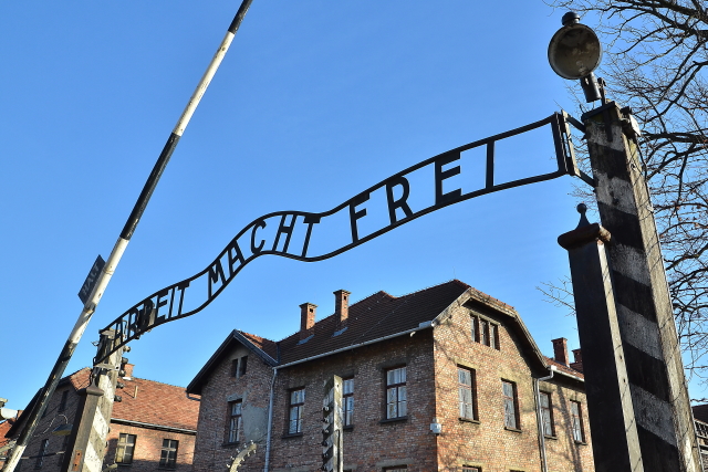 Brána koncentračního tábora v Osvětimi s nápisem Arbeit macht frei.