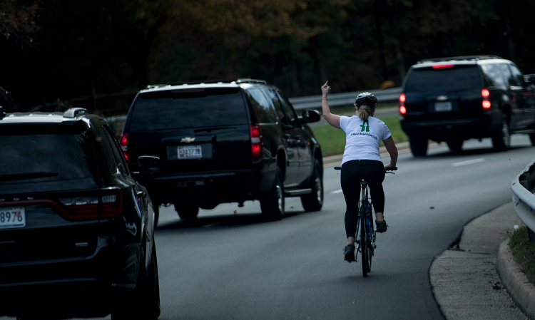 Žena ukazující prostředníček autokoloně amerického prezidenta Donalda Trumpa.