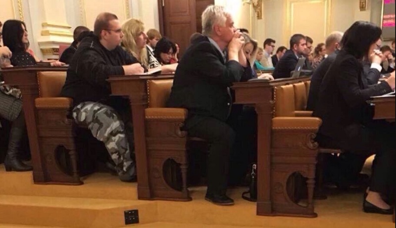 Muž v maskáčových kalhotách v lavici sněmovny.