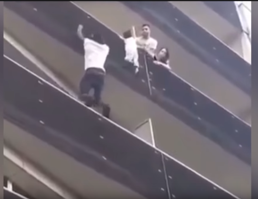 Statečný Malijec zachraňuje dítě, které visí z balkonu.