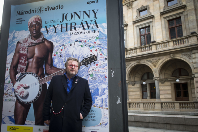Divadelní režisér David Drábek pózuje před plakátem s obnaženým černošským muzikantem, jehož vypracované tělo zakrývá jen bendžo.