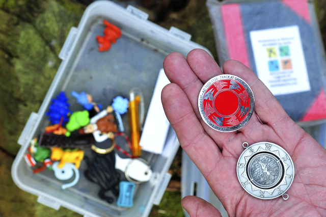 Jak vypadá "keška". Krabička obsahuje drobnosti na výměnu, dva geocoiny, které se po nálezu vloží do jiné nalezené keše, a sešit k zapsání nálezu.