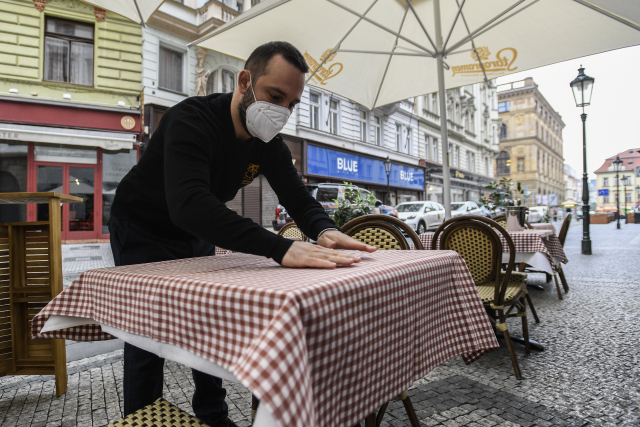 Číšník prostírá stůl na zahrádce restaurace v centru Prahy.