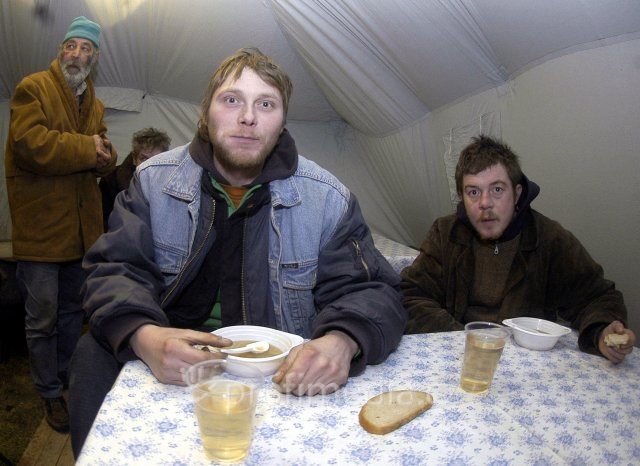 Slovenští bezdomovci si pochutnávající si na jídle od charity.