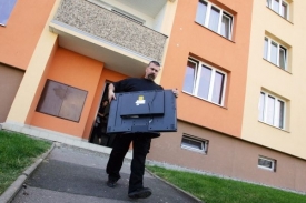 Správce daně odnáší z bytu dlužníka zabavenou televizi.