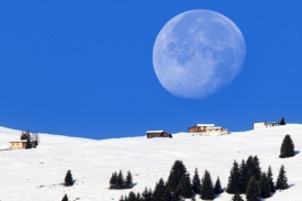 Obrovsk&yacute; měs&iacute;c nad zasněženou chatou ve &scaron;v&yacute;carsk&yacute;ch Alp&aacute;ch.