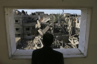 Palestinec se d&iacute;v&aacute; ze sv&eacute;ho bytu na rozbombardovan&eacute; okol&iacute;.