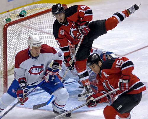 Brian Gionta (14) z New Jersey Devils' přeskakuje Cristobala Hueta z Montreal Canadiens a Michael Komisarek (vlevo) a Jamie Langenbrunner (15) za New Jersey během druhé třetiny středečního zápasu NHL.
