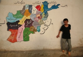Afgh&aacute;nsk&yacute; sirotek stoj&iacute; před mapou Afgh&aacute;nist&aacute;nu.