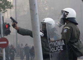 Policista míří na útočící demonstranty pistolí.